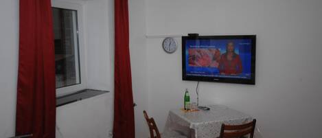 A small room with a bed, a table with a TV, and a window with red curtains.