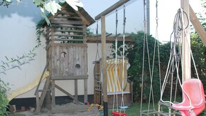 A wooden play structure with a slide, a swing, and a climbing ladder. - Airportgästehaus Bremen (Bremen)