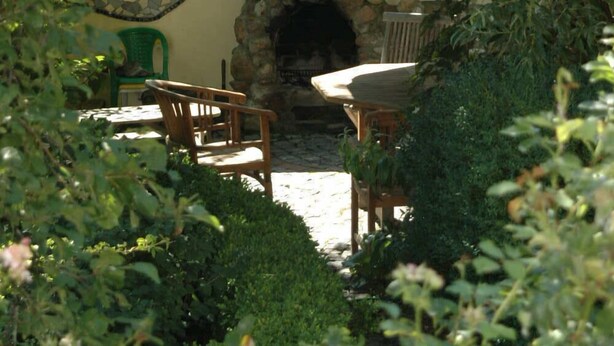 An outdoor patio with stone walls, a stone fireplace, and wooden furniture. - Airportgästehaus Bremen (Bremen)