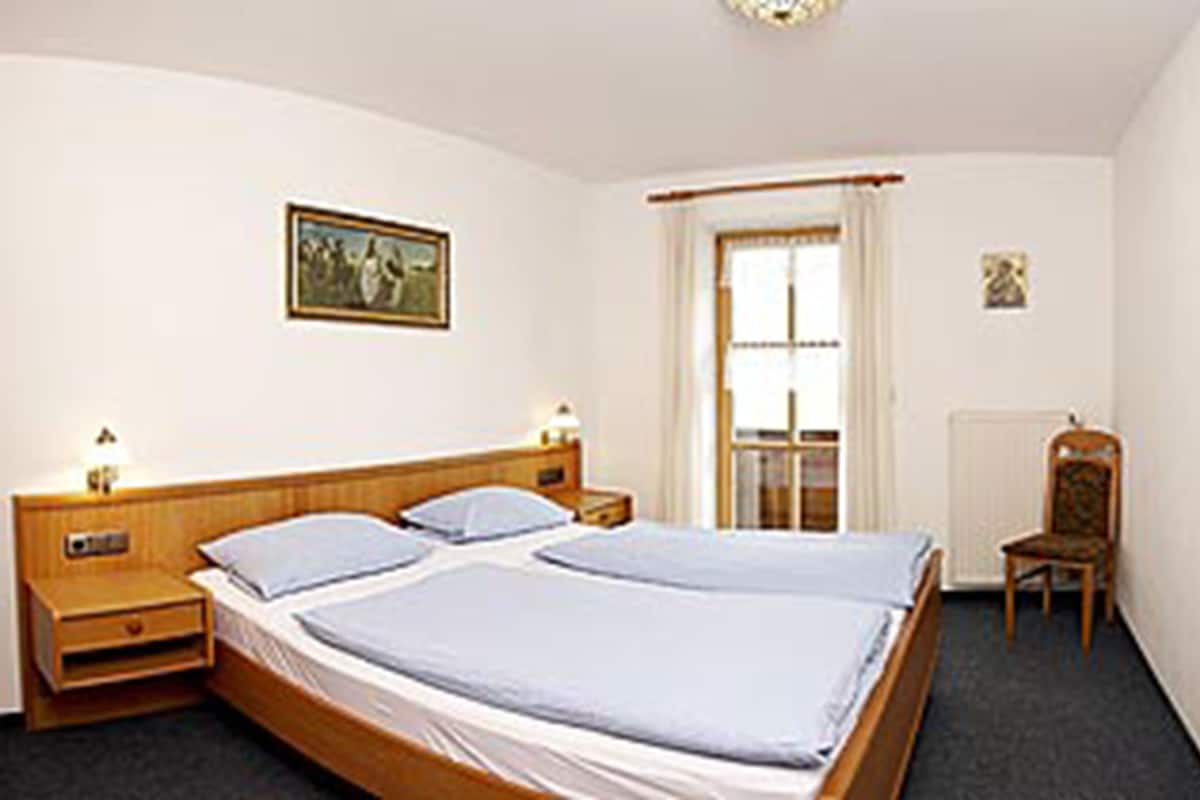 A hotel room with a double bed, two bedside tables, a chair, a window with curtains, and a painting on the wall.
