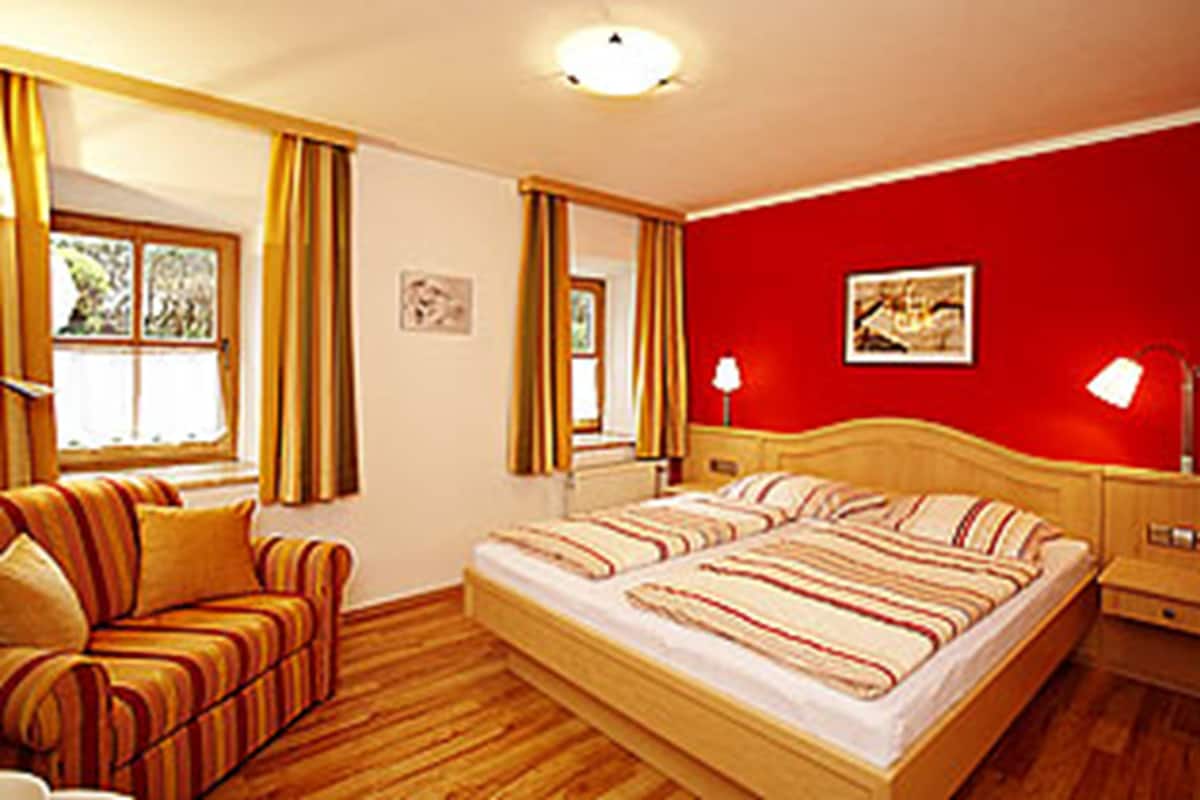 A bedroom with a double bed, a bedside table with a lamp, a chair, and a window with curtains.