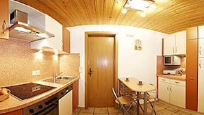 A compact kitchen with a stove, sink, and microwave. There is a wooden door and a small dining table with chairs. - Beim Draxl (Reit im Winkl)