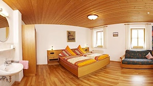 A spacious bedroom with a wooden ceiling, a large bed, a sofa, a small table, and a window. - Beim Draxl (Reit im Winkl)