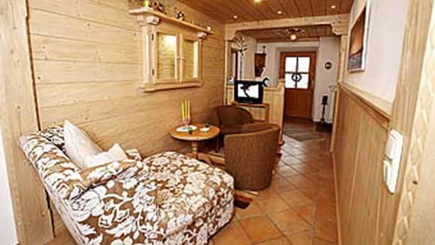 A cozy room with a wooden floor, a sofa with a floral cushion, a small round table with a candle, and a chair. - Beim Draxl (Reit im Winkl)
