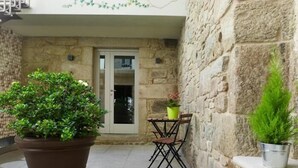 A stone-walled patio with a large potted plant, a small table with two chairs, and a door leading to an interior space. - Hotel Real Cambados (Cambados)