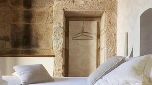 A bedroom with a stone wall, a hanging light fixture, and a bed with pillows. - Hotel Real Cambados (Cambados)