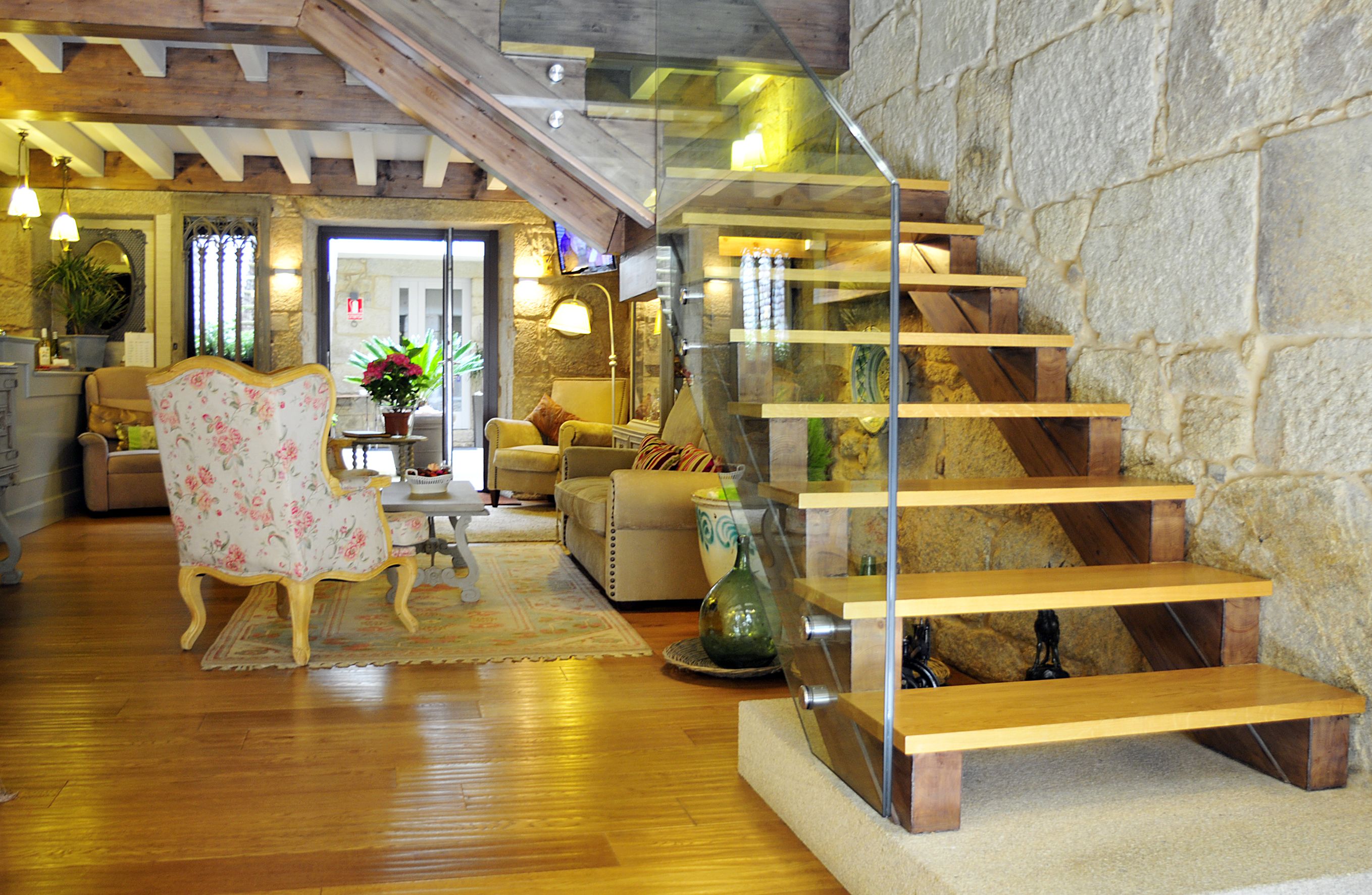 Un salón amplio con una escalera de madera, un sillón estampado y una pared de piedra.