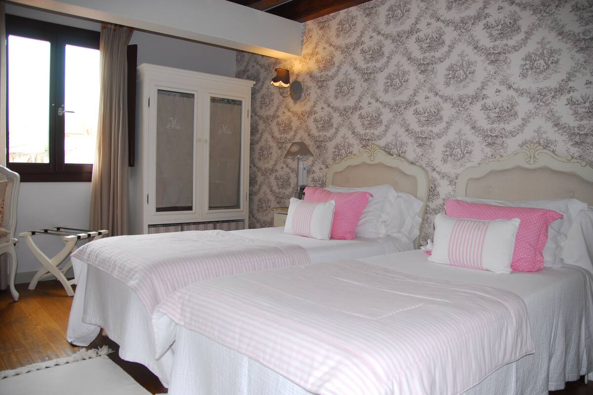 A bedroom with two beds, a wardrobe, a chair, and a window with curtains.