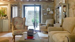 A cozy living room with a wooden ceiling, a stone wall, and a large window. There are two armchairs, a sofa, and a coffee table. - Hotel Real Cambados (Cambados)