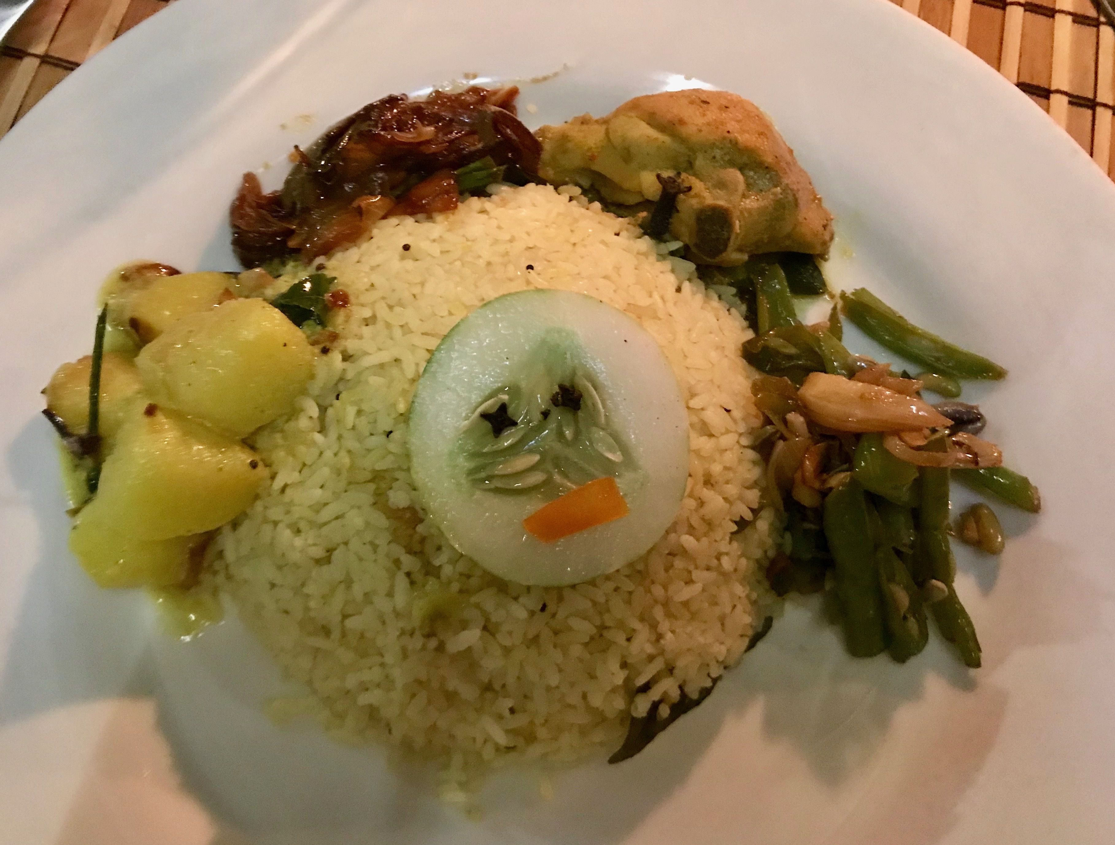 Un plato con arroz, una rodaja de pepino, judías verdes y un trozo de carne.