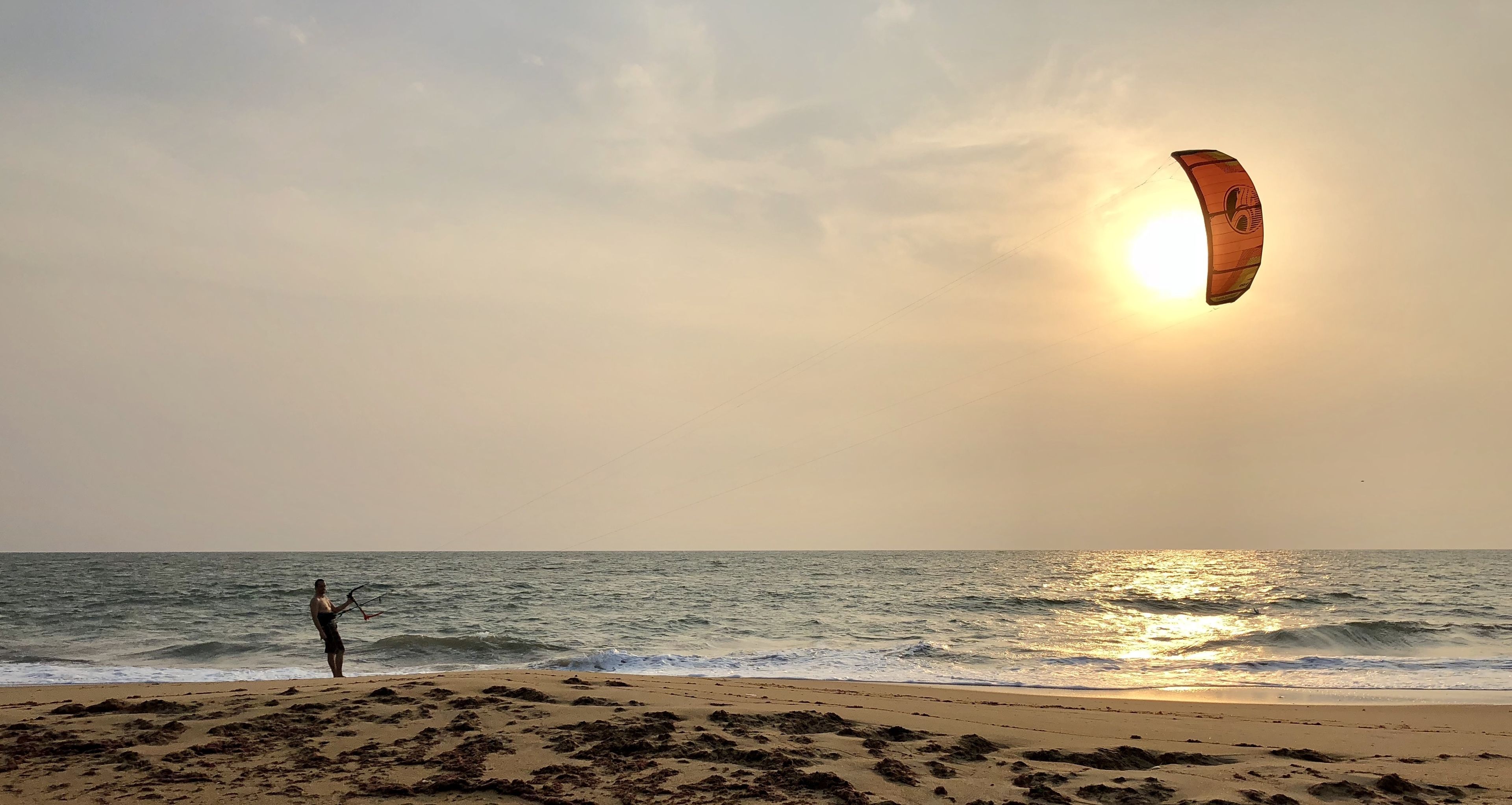 A beach scene with a person flying a kite near the water.