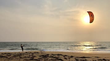 A beach scene with a person flying a kite near the water.