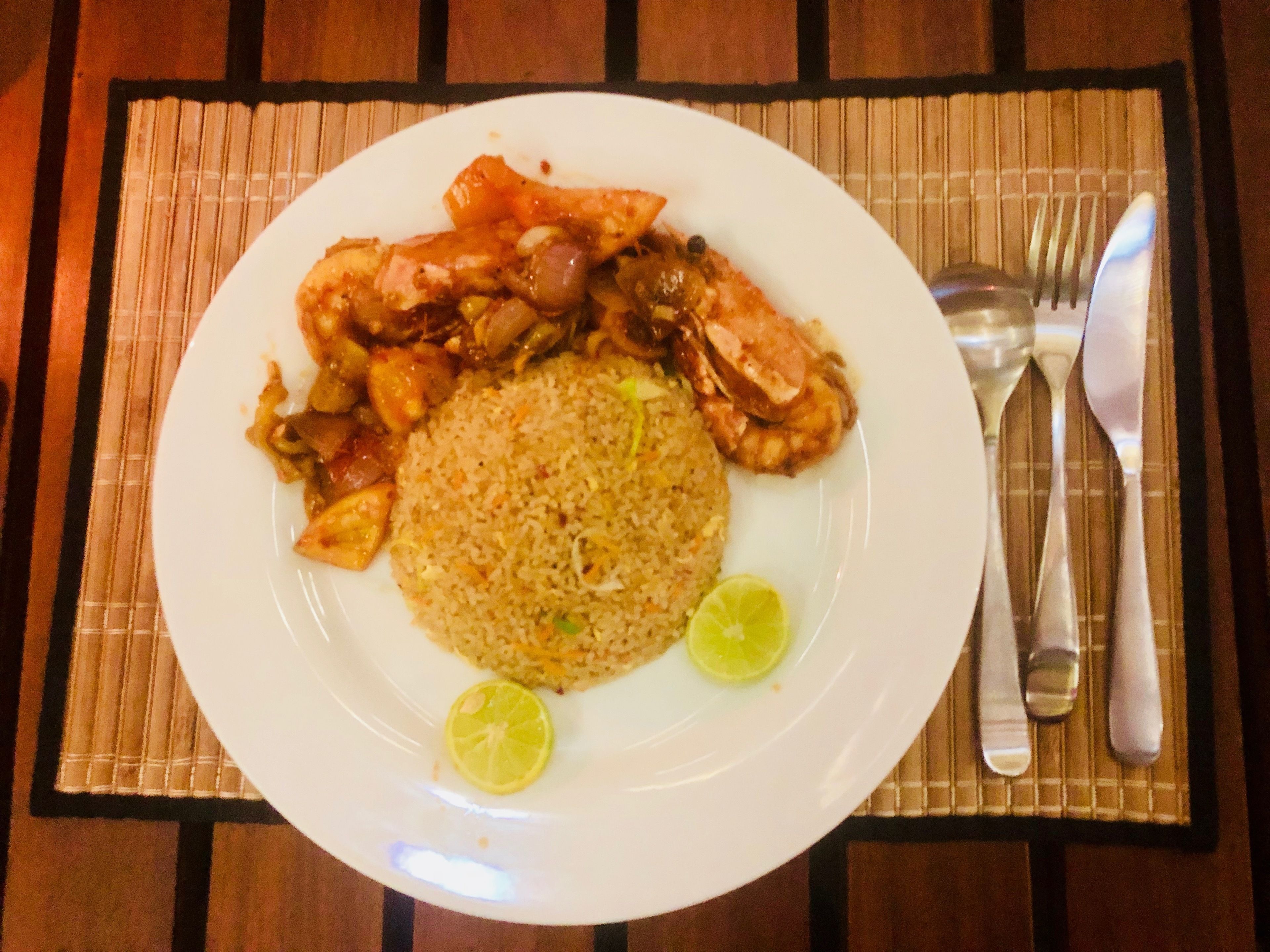 A plate of fried rice with chicken and lime wedges on a white plate, placed on a bamboo mat.