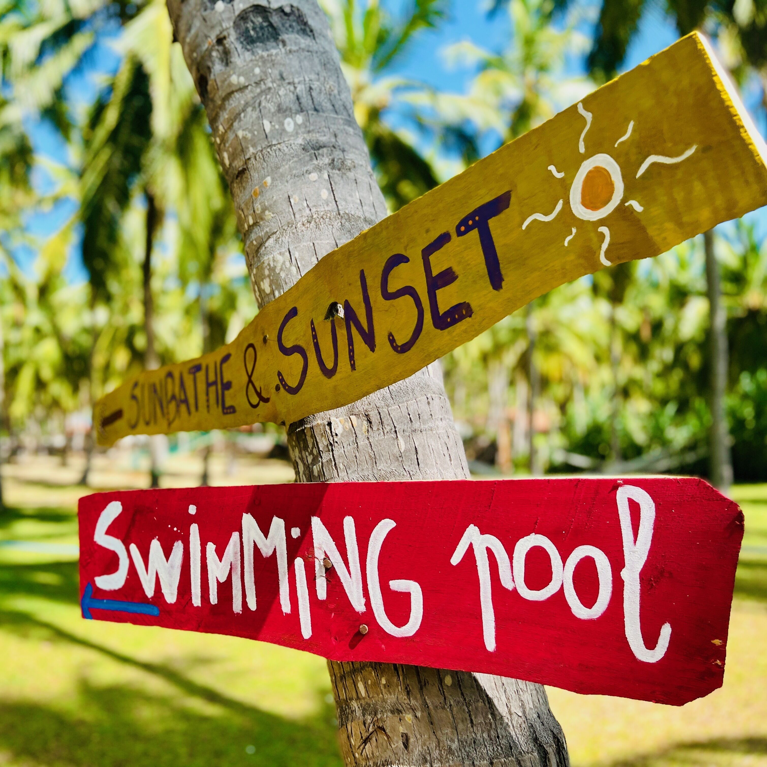 A wooden signpost with two signs: one pointing to 'SUNGATE & SUNSET' and another to 'Swimming Pool'.