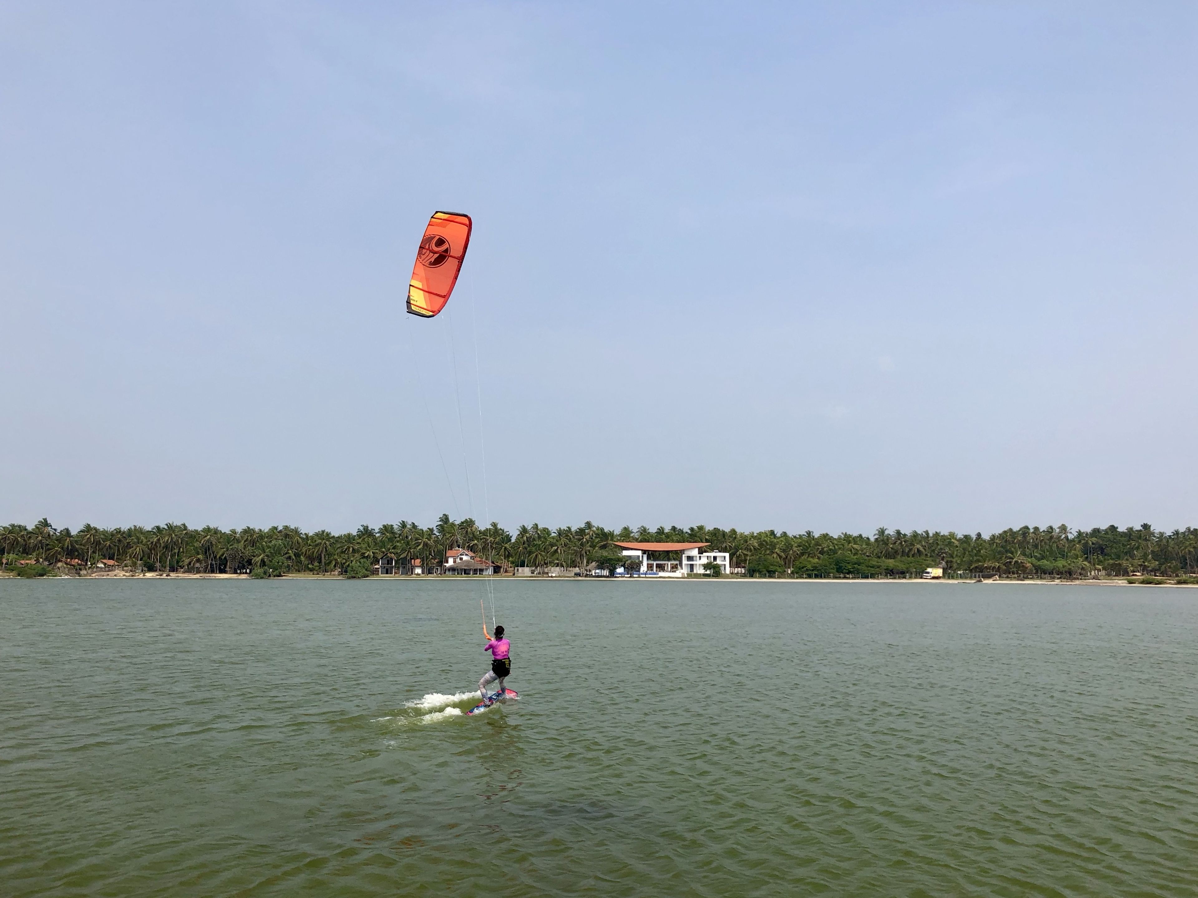 A person windsurfing on a calm body of water with a clear sky.