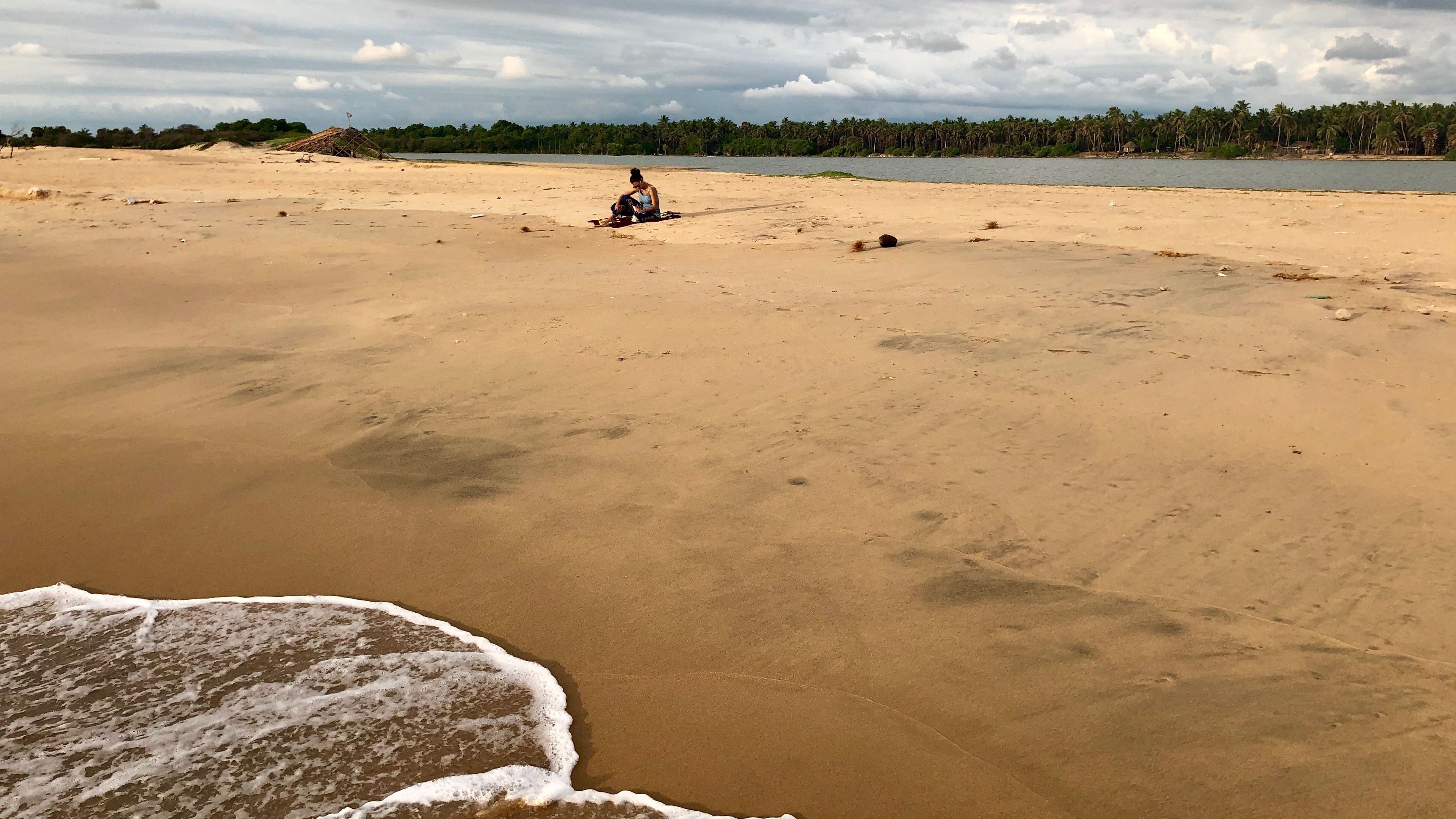 Una extensa playa arenosa con un mar tranquilo, algunas rocas dispersas y una línea distante de árboles.