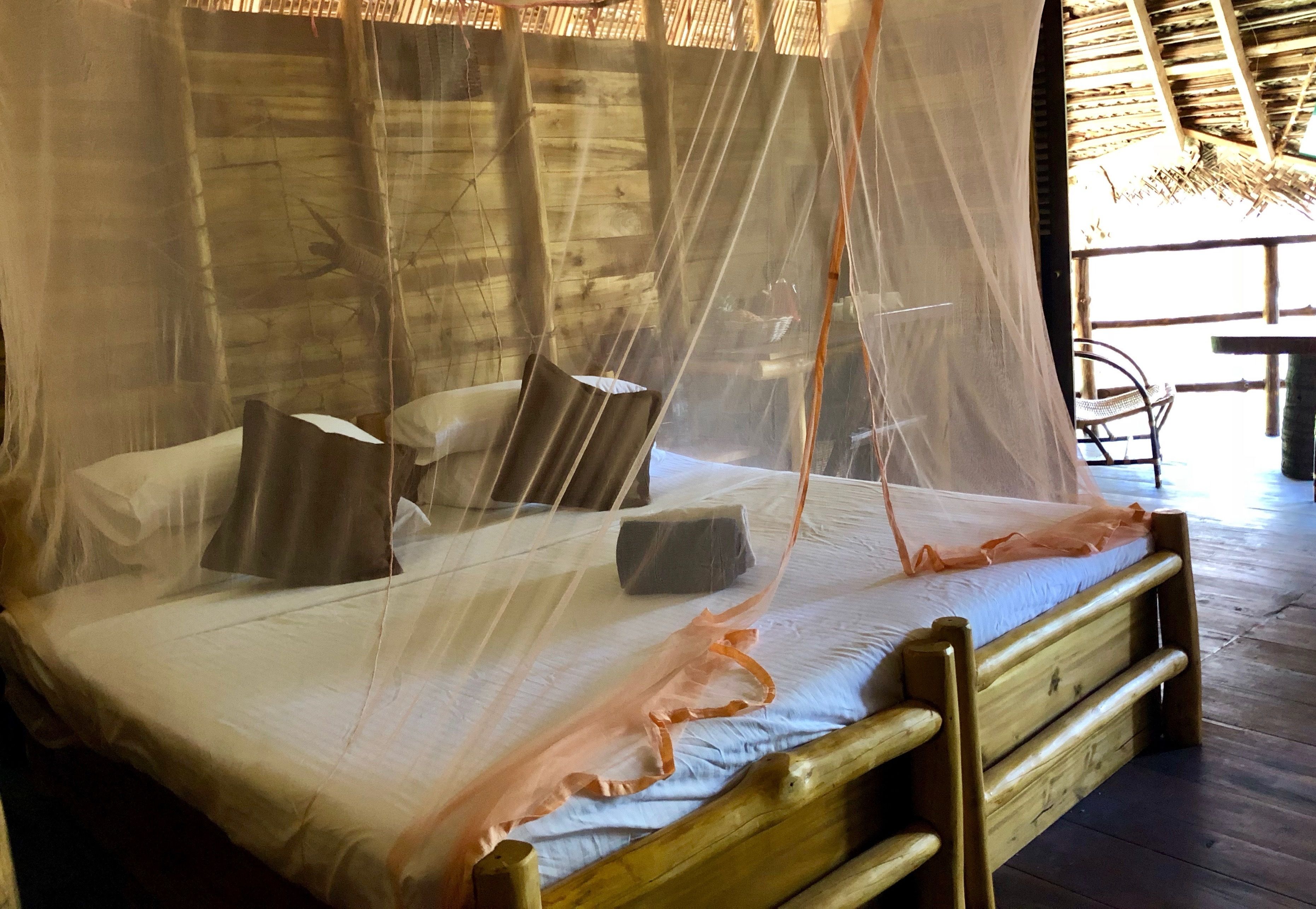 A wooden bed with a mosquito net, pillows, and a wooden headboard.