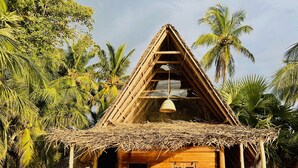 A wooden hut with a thatched roof, a woven fence, and a bench outside.