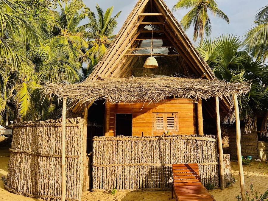 A wooden hut with a thatched roof, a woven fence, and a bench outside.