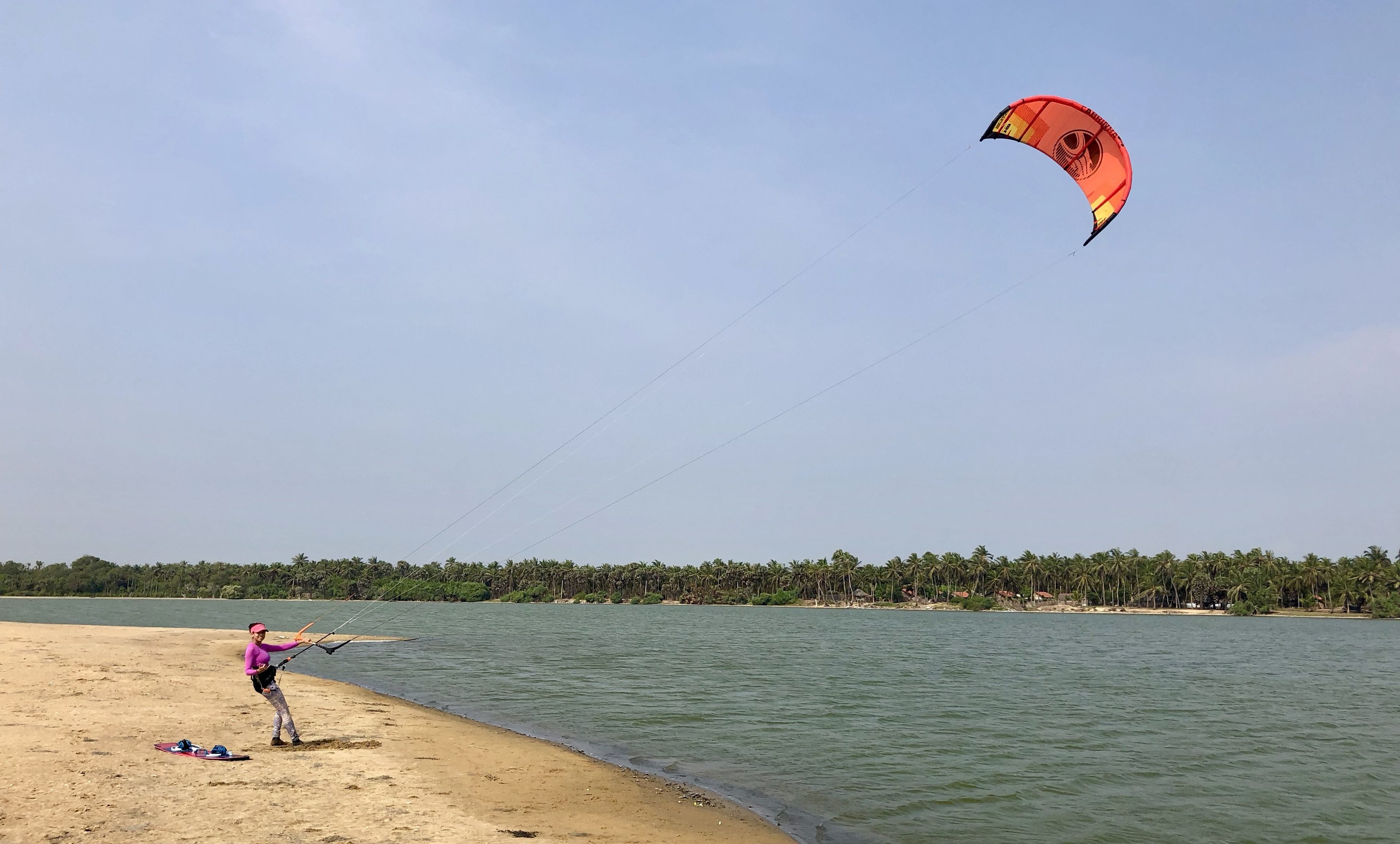 A beach scene with a person flying a kite near the water's edge.