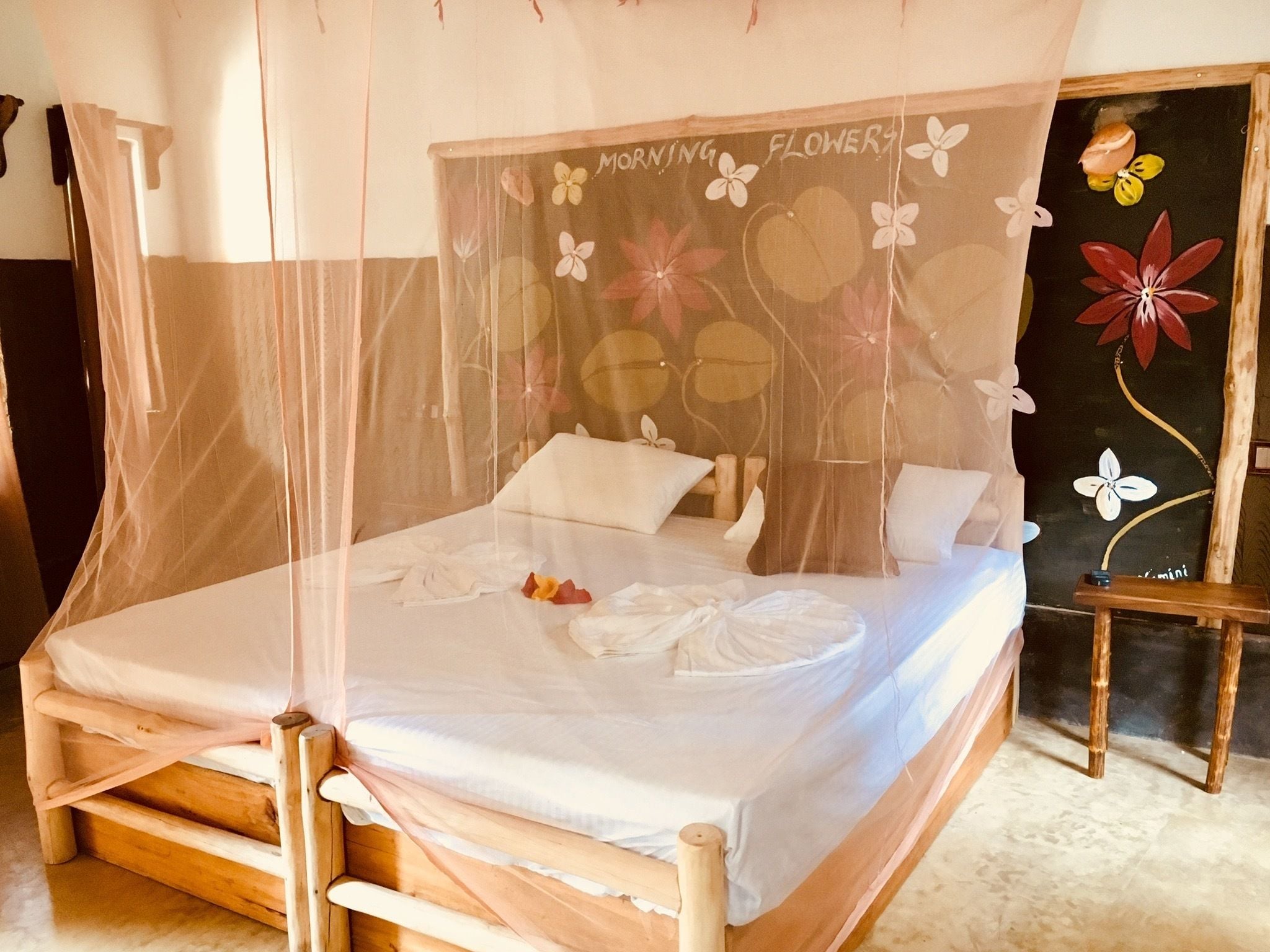 Una cama con dosel, cabecera de madera y pared con un cuadro floral.