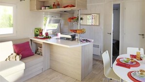 A compact kitchen with a central island, a dining area with a white table, and a cozy seating area with a sofa. - Camping Le Diben (Larmor-Baden)