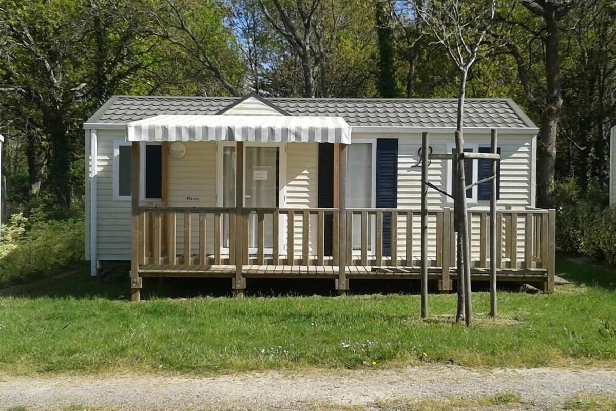 A small, single-story mobile home with a porch and a fenced deck area.