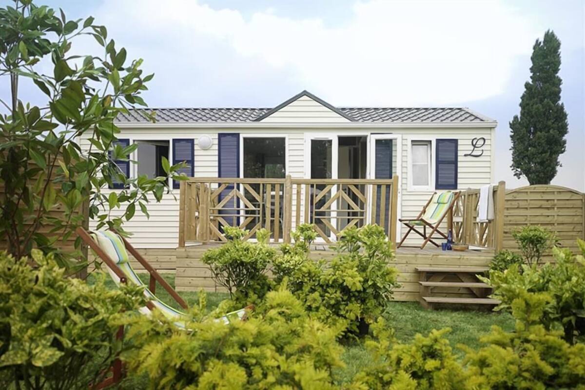 A mobile home with a fenced backyard, a slide, and a deck with chairs.