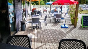 An outdoor patio with wooden flooring, tables, chairs, and umbrellas. - Camping Le Diben (Larmor-Baden)