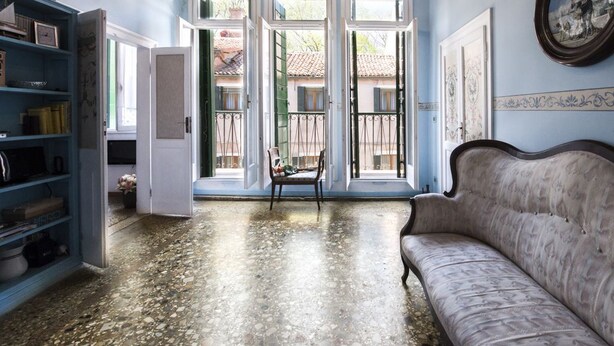 A room with a sofa, a bookshelf, and a chair near large windows. - Venice Giardini Biennale Apartment (Venice)