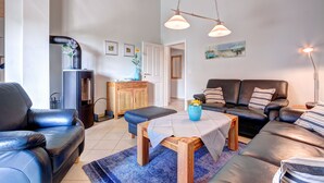 A living room with a black leather sofa, a wooden coffee table, and a blue vase. There is a fireplace with a black chimney, a wooden cabinet, and a door leading to another room. - Ferienpark Am Meer Klipper (Butjadingen)