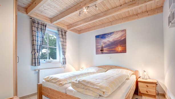 A bedroom with a wooden bed, a nightstand, a painting, and a window with curtains. - Ferienpark Am Meer Klipper (Butjadingen)