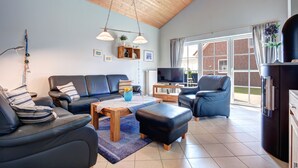 A modern living room with a sofa set, a coffee table, and a TV. There is a wooden ceiling and a window with curtains. - Ferienpark Am Meer Klipper (Butjadingen)