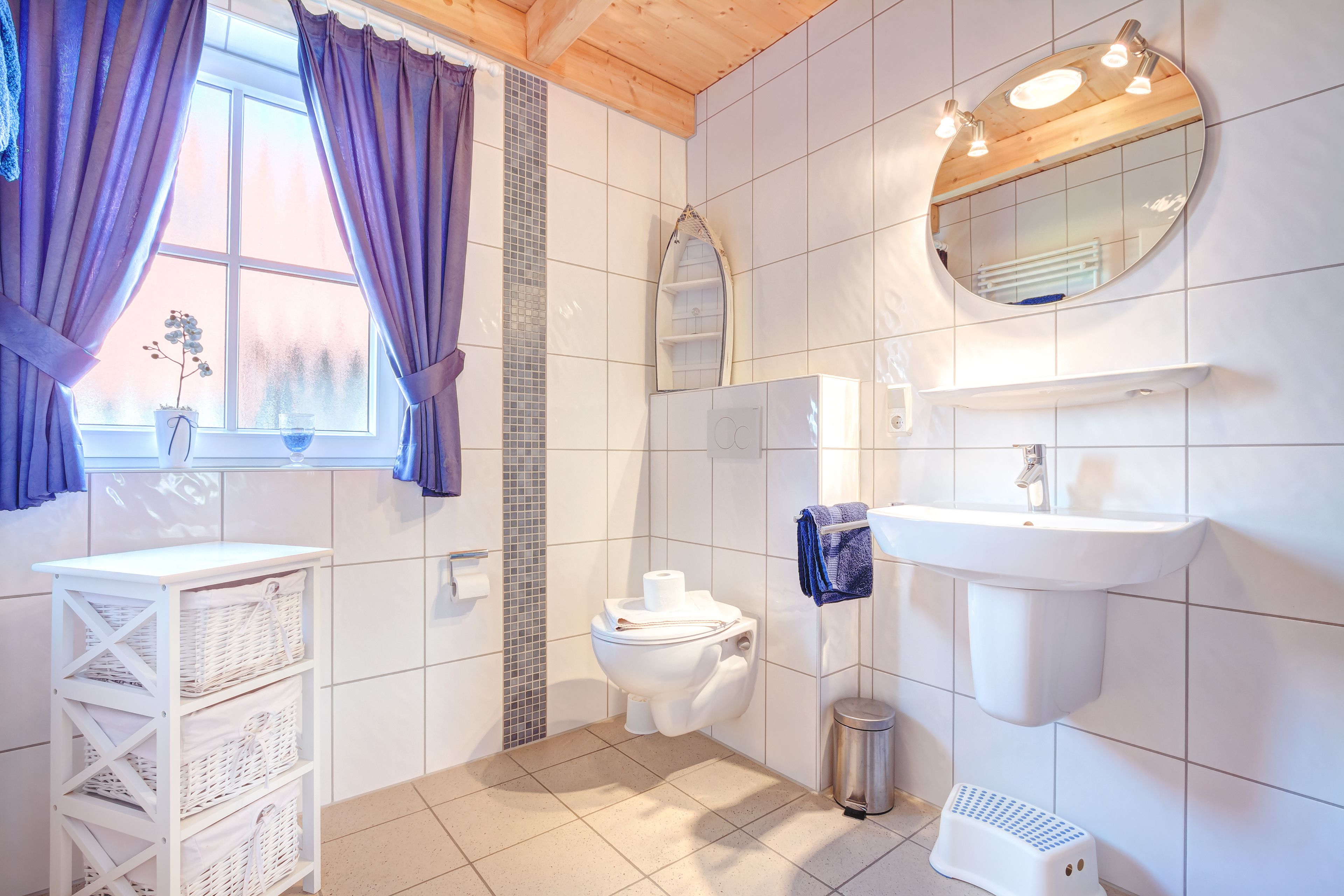 Une salle de bain équipée de toilettes, d’un lavabo, d’un miroir et d’une fenêtre avec des rideaux.