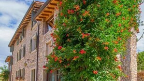 Un edificio de piedra con un balcón de madera y un árbol con flores rojas.