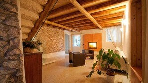 Una sala de estar acogedora con pared de piedra, vigas de madera, chimenea y asientos cómodos.