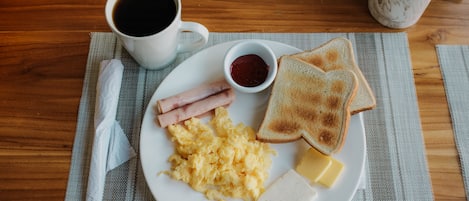 Un plato de desayuno con huevos revueltos, tocino, tostadas, mantequilla y mermelada sobre una mesa de madera.