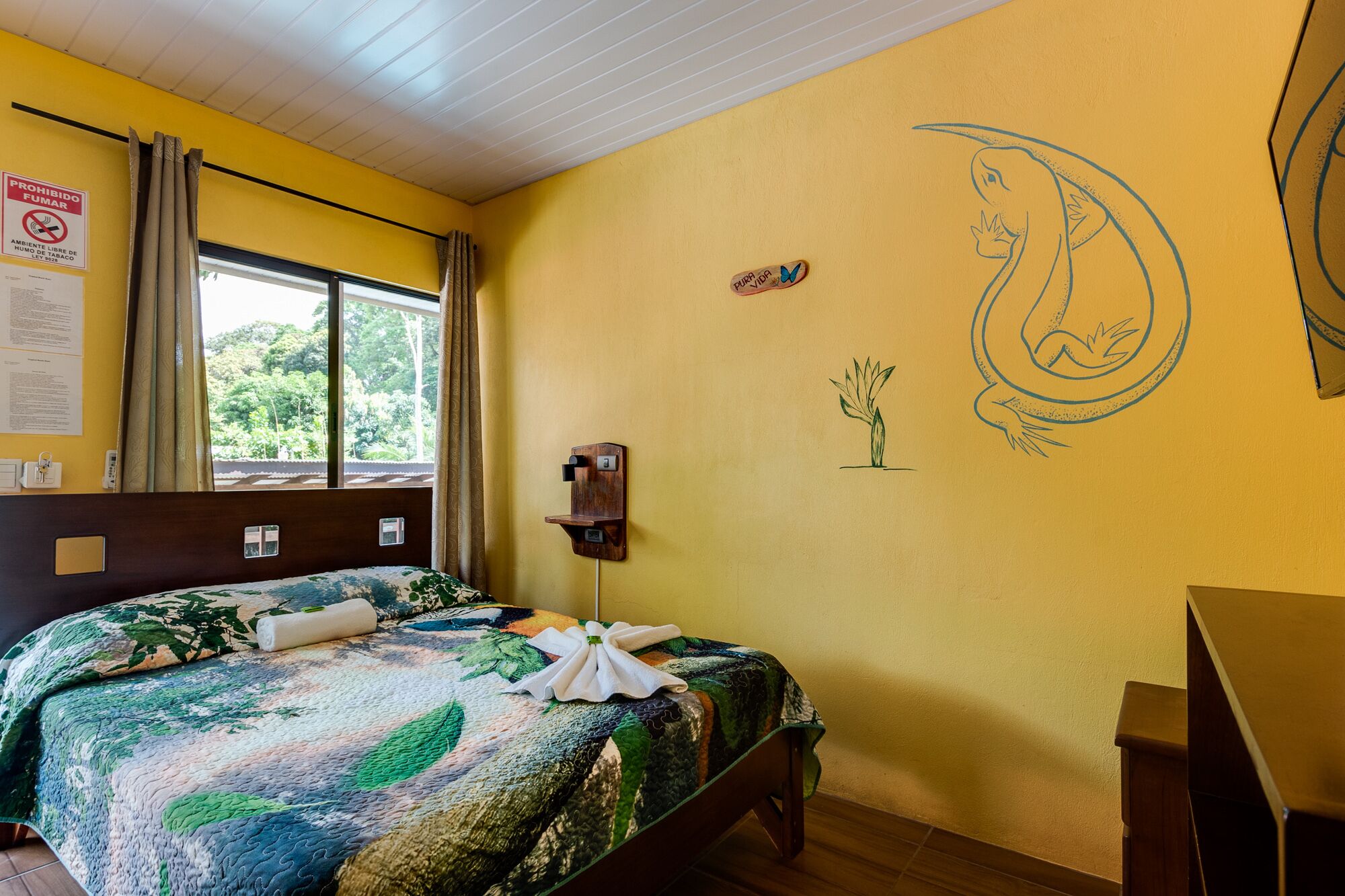 A room with a bed, a window, a wall-mounted shelf, and a wall decoration.