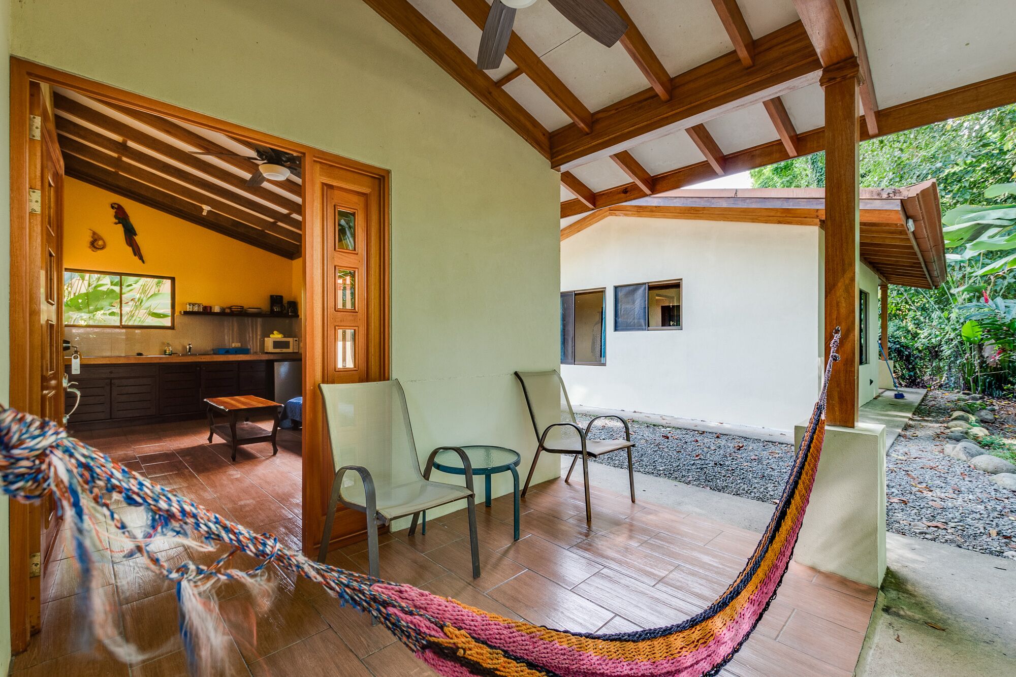 A hammock in a covered outdoor area with a view of a house and garden.