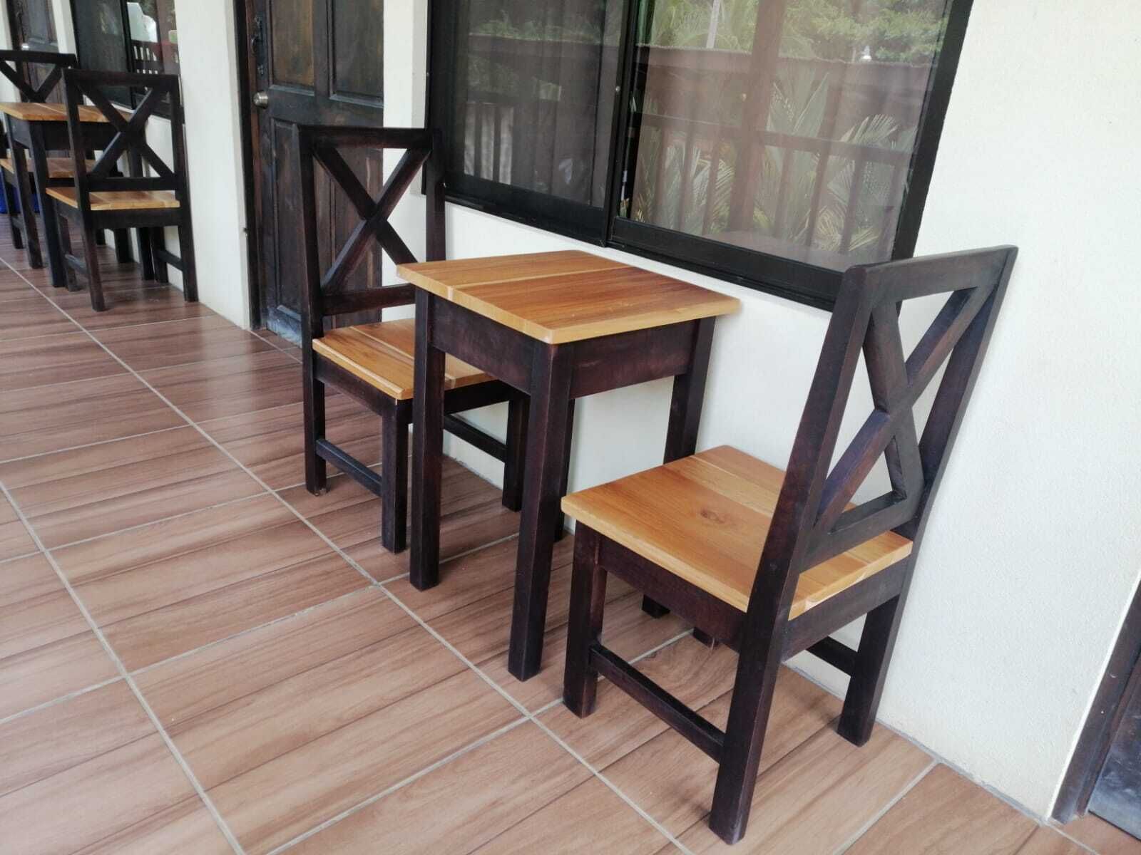 Una fila de mesas y sillas de madera, con piso de baldosas, ubicada cerca de una ventana que da a zonas verdes.