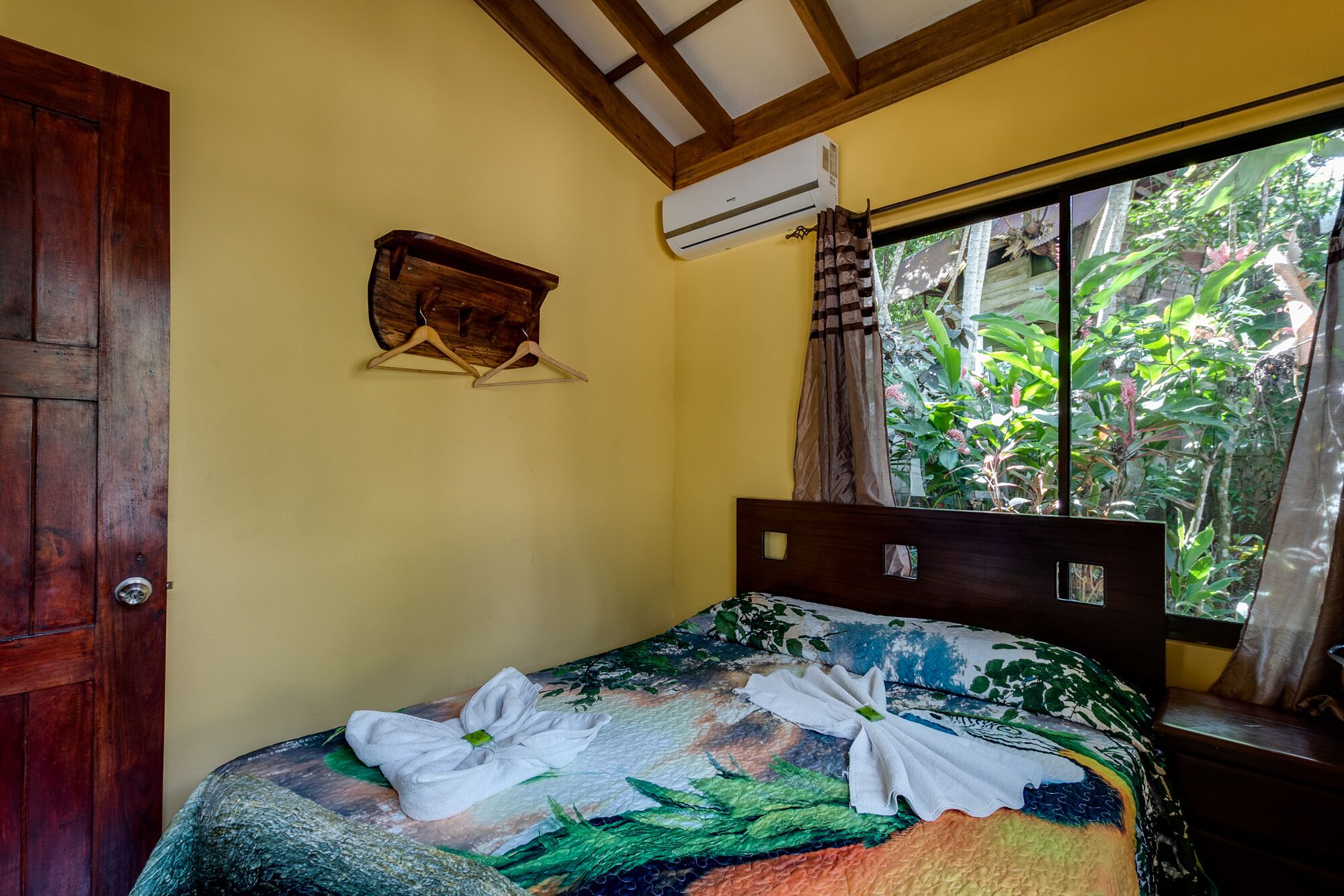 A room with a bed, a wooden door, an air conditioning unit, and a window with curtains.