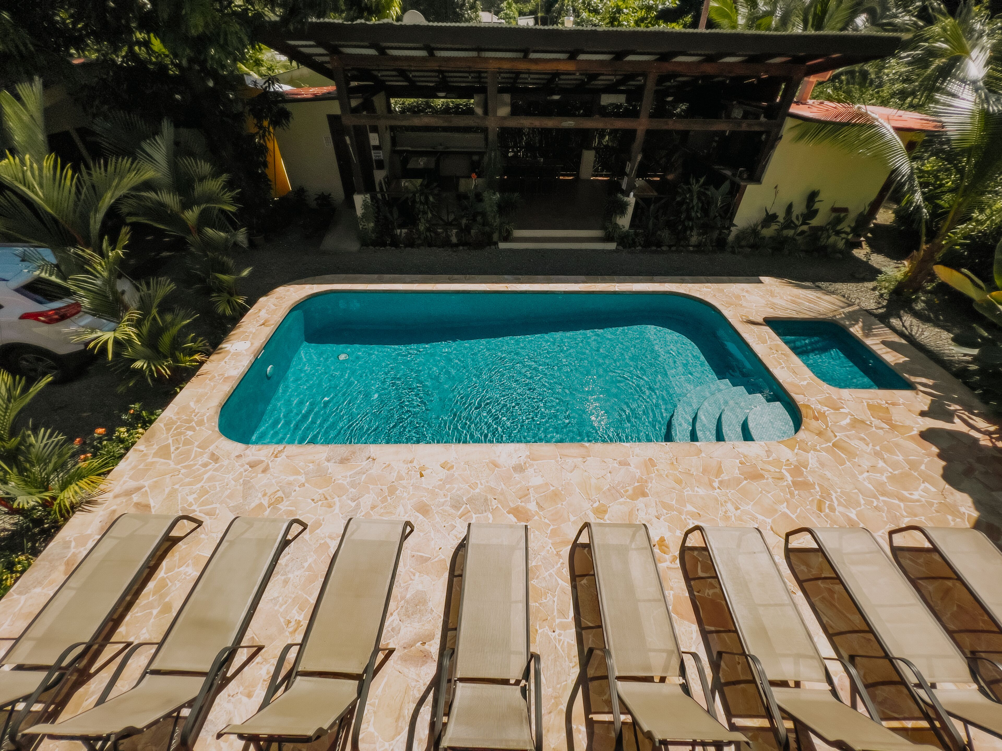 A swimming pool with lounge chairs in the foreground and a covered area in the background.
