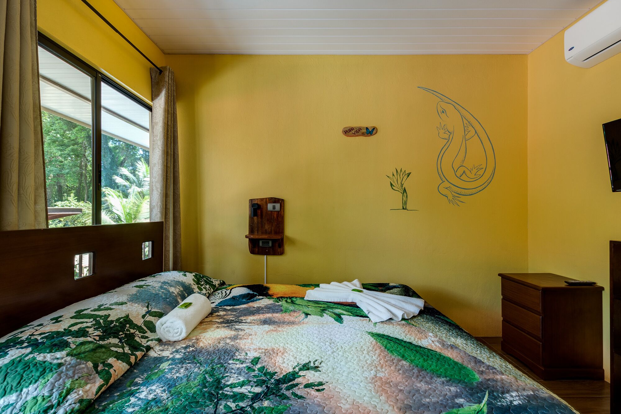 A room with a bed, a wooden nightstand, a wall-mounted telephone, and a window with curtains.