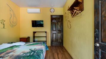 Un dormitorio con cama, televisión, aire acondicionado, puerta de madera y un reloj de pared.