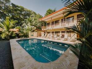A pool area with lounge chairs, a two-story building with balconies, and surrounding tropical vegetation. - Tropical Beach (Bahía Ballena)