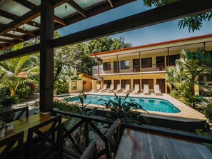 A poolside view of a hotel with a pool, lounge chairs, and a two-story building with balconies. - Tropical Beach (Bahía Ballena)