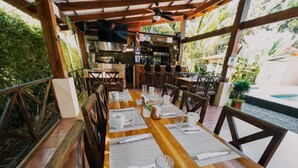 Un restaurante con mesas y sillas de madera, una zona de bar y vistas a zonas verdes.