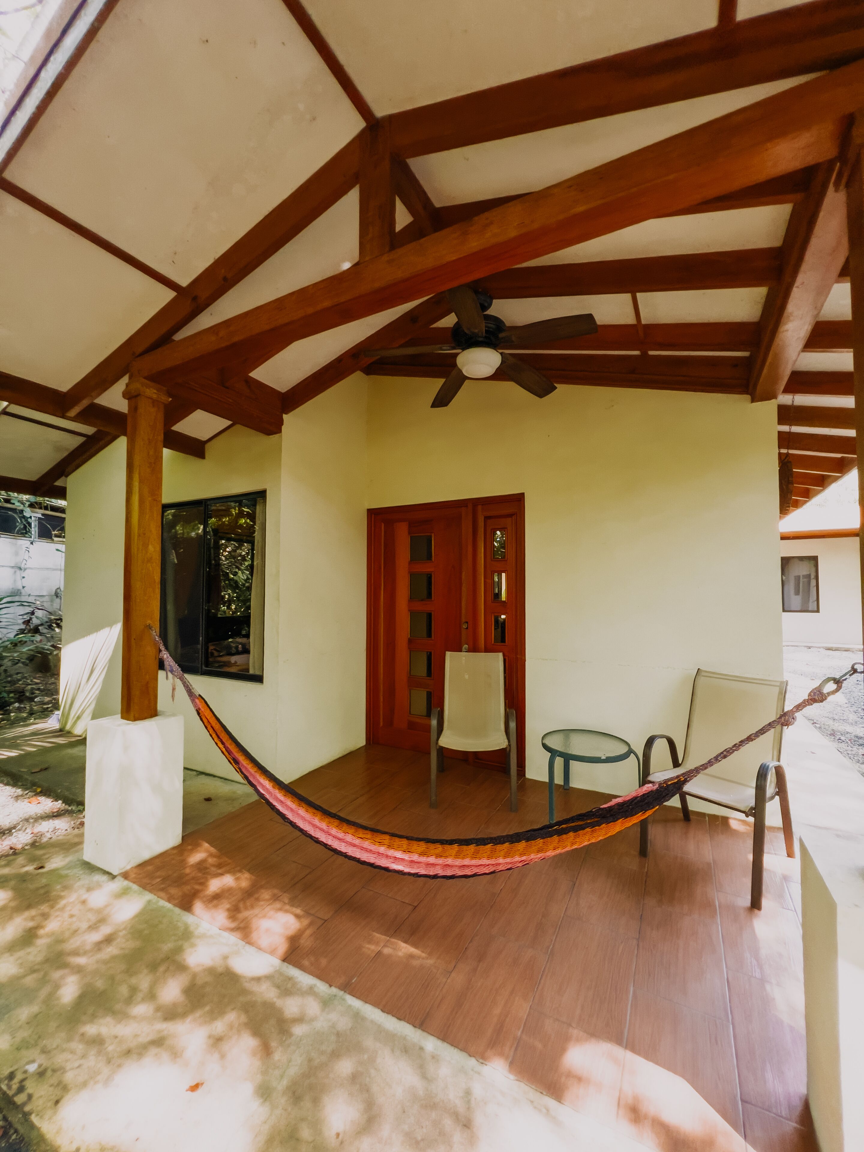 A covered outdoor area with a hammock, wooden beams, a ceiling fan, and a door with glass panels.