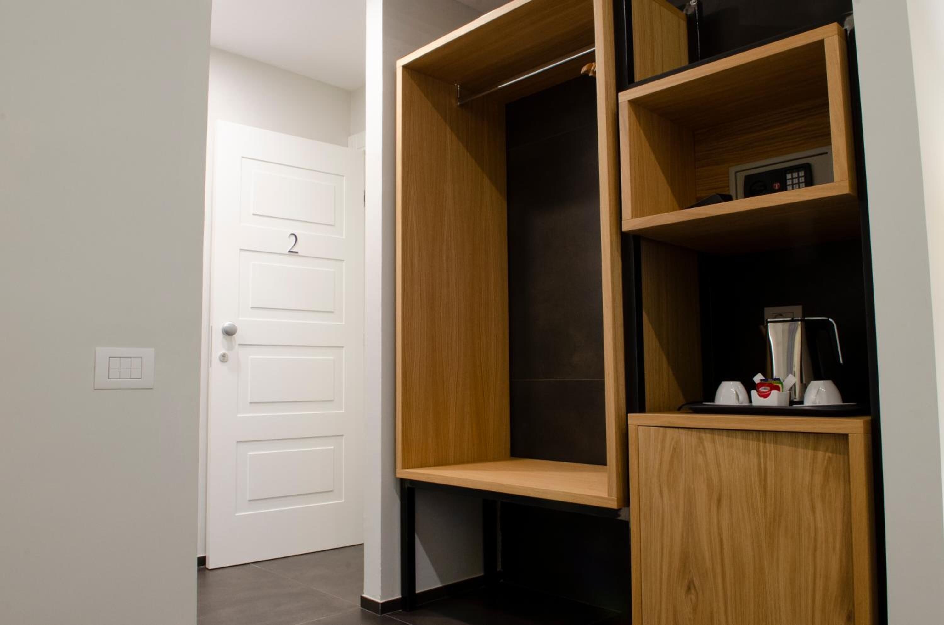 A modern closet with a wooden finish, a black door, and a shelf with a coffee maker and cups.