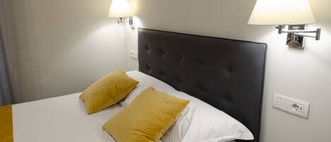 A hotel room with a bed, two pillows, a nightstand, and two wall-mounted lamps.